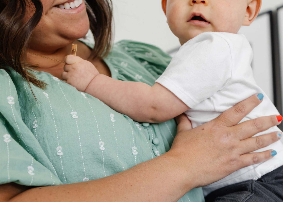 Close-up of a baby in a white onesie resting against a parent wearing a green shirt with floral patterns, showing comfort and bonding.
