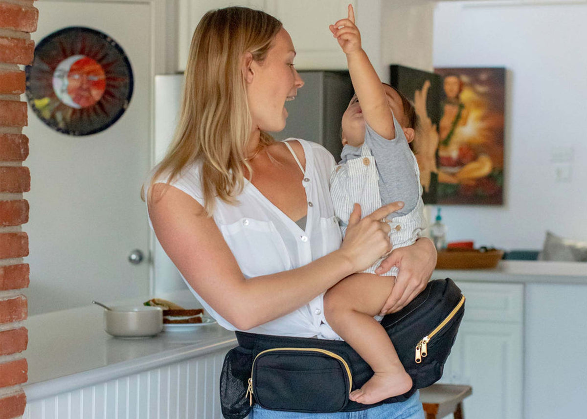 a mom using tushbaby hip carrier to carry her baby