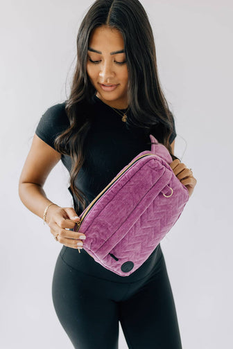 Adult unzipping the main compartment of The Pack in Orchid while wearing it across the chest