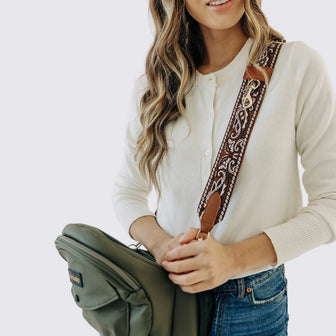 Close-up of an adult carrying a folded Vegan Leather Olive Tushbaby Hip Carrier with The Crossbody Strap in Cowboy
