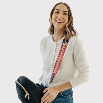 Smiling adult carrying a folded Black & Gold Tushbaby Hip Carrier across the body with The Crossbody Strap in Zigzag