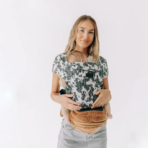 Adult carrying a sleeping baby facing inward in an Abstract Hip Seat Hands-Free Attachment with a Velvet Sable Tushbaby Hip Carrier