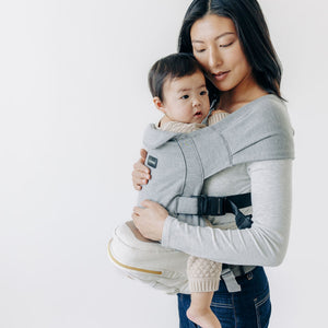 Adult carrying a baby in a Grey Snug Attachment against a white background