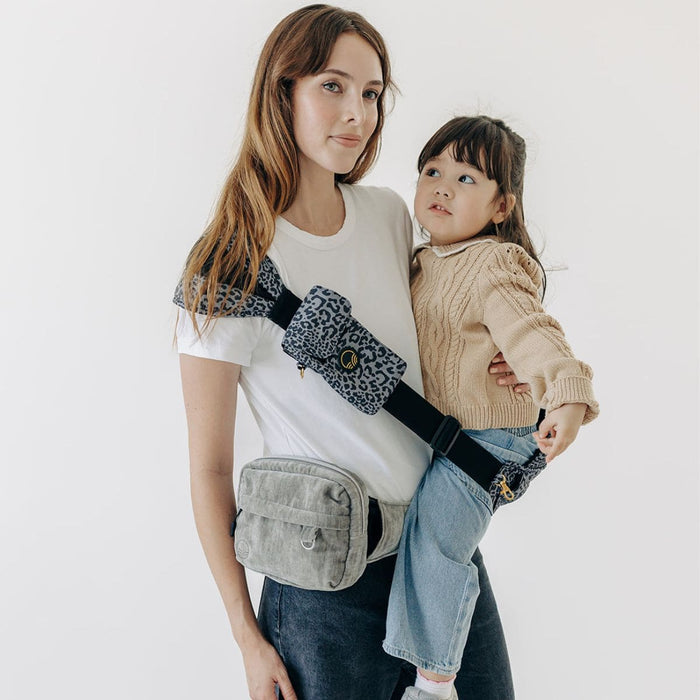 Adult carrying a child in the Jaguar Tushbaby Liftoff Toddler Sling while wearing a Silver Mini Pack